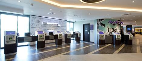A modern hotel lobby with check-in kiosks, a large wall with motivational quotes, and a circular light fixture.