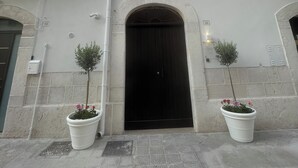 A two-story building with a black entrance door, white walls, and a balcony on the upper floor. - Blanco Group (Trani)