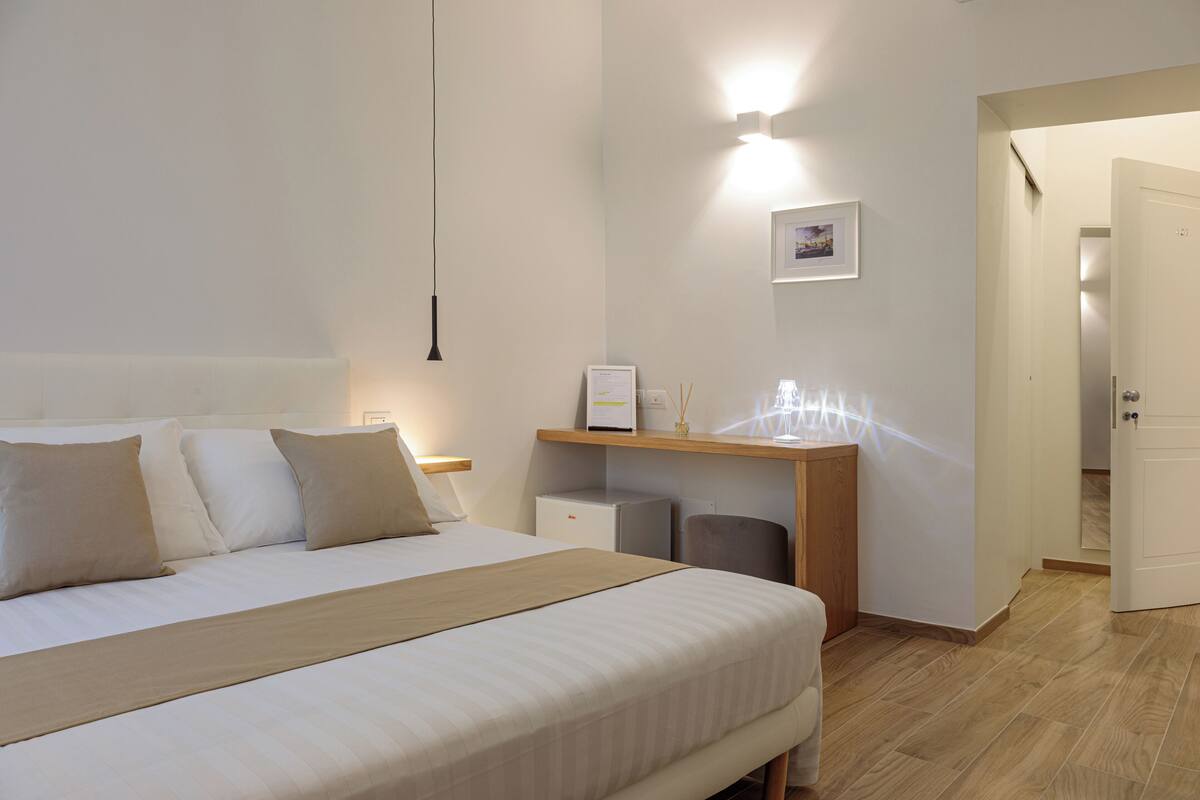 A neatly arranged bedroom with a bed, bedside table, and a small desk with a chair.