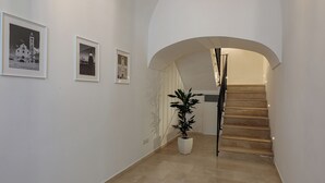 A hallway with a staircase, white walls, and framed pictures. - Blanco Group (Trani)