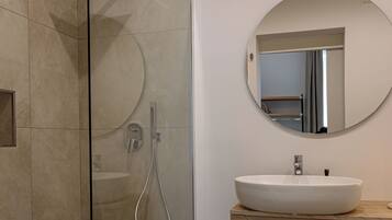 A modern bathroom with a glass-enclosed shower, a round mirror, and a wooden vanity.