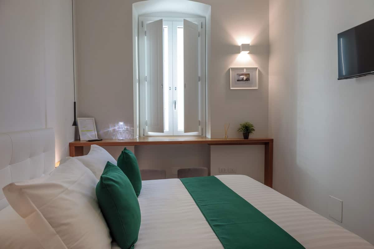 A hotel room with a bed, a desk, a chair, a TV, and a window with blinds.