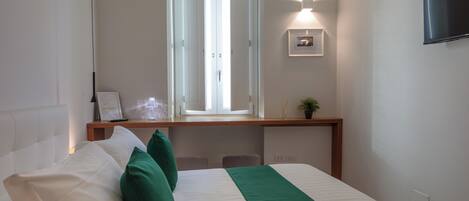A hotel room with a bed, a desk, a chair, a TV, and a window with blinds.