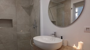 A modern bathroom with a large oval sink, a round mirror, and a wooden vanity. - Blanco Group (Trani)