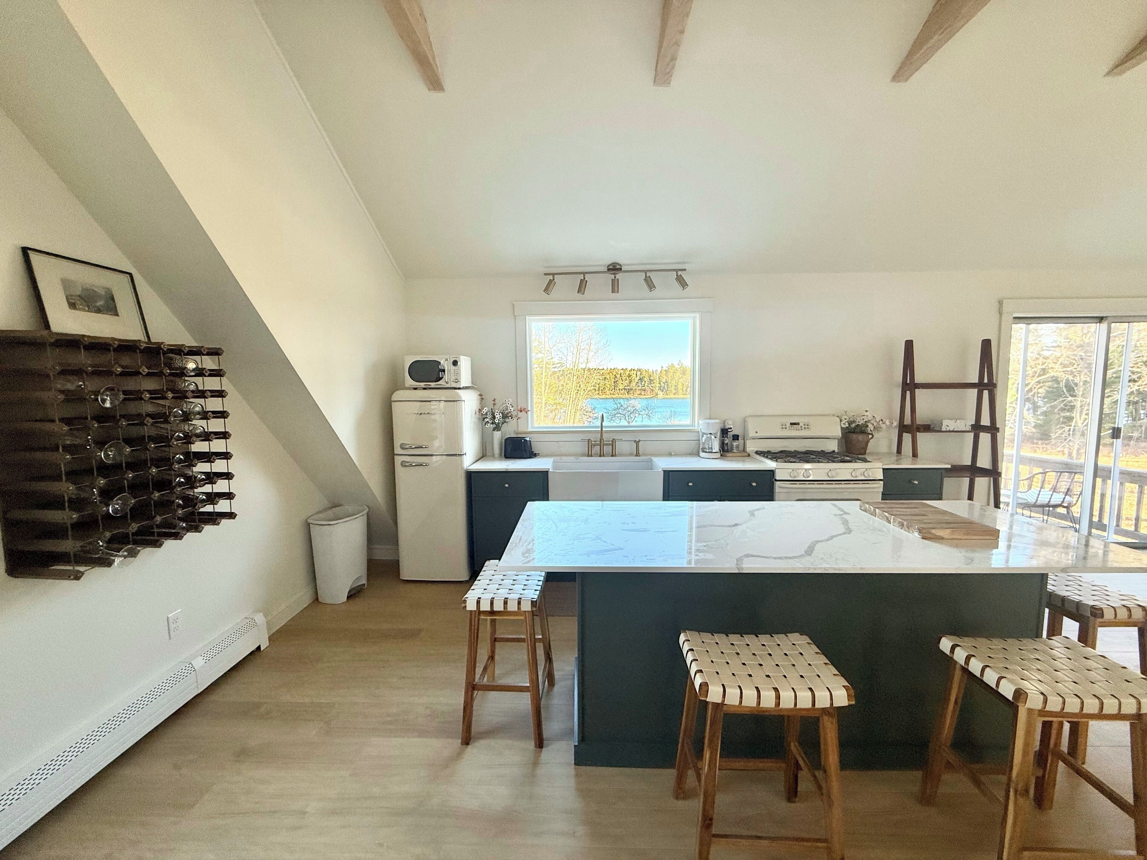 A kitchen with a central island, bar stools, a refrigerator, and a window with a view.