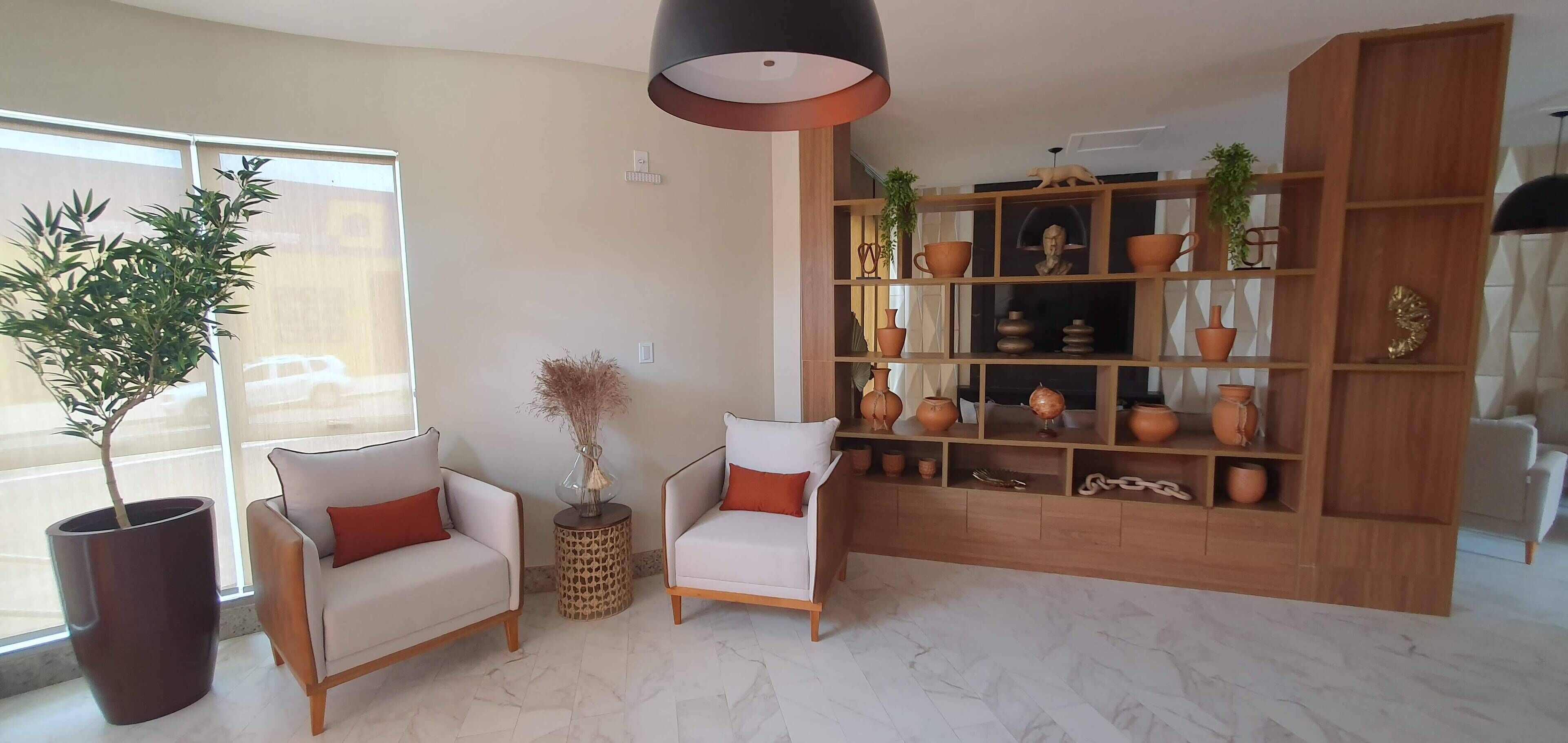 A living room with two armchairs, a large potted plant, a wooden bookshelf filled with decorative items, and a modern pendant light.
