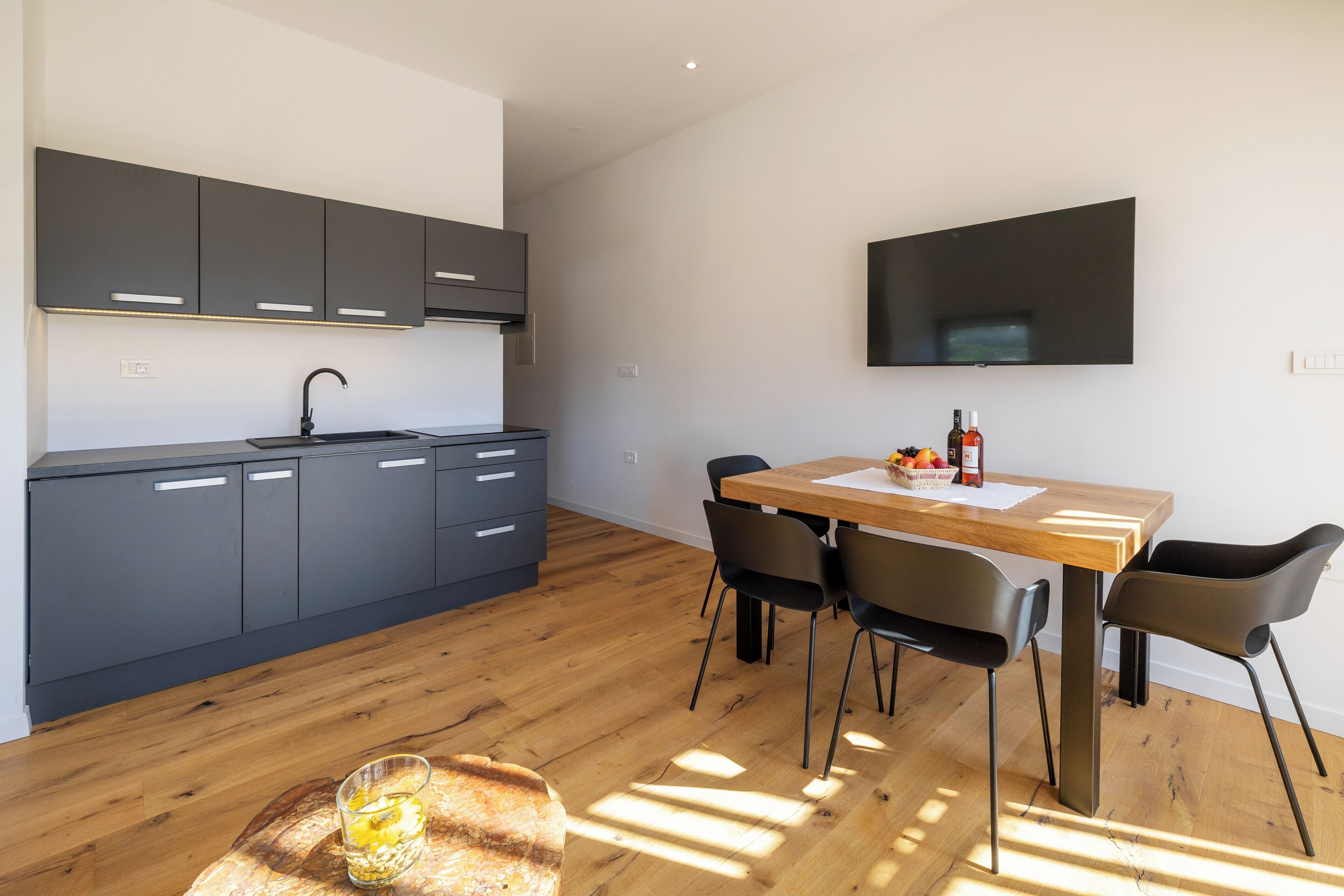 A modern kitchen with dark cabinets, a wooden dining table, and black chairs.