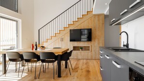 A modern kitchen with a wooden staircase, a dining area with chairs, and a built-in TV. - Winery and Apartments Marof (Bistrica ob Sotli)