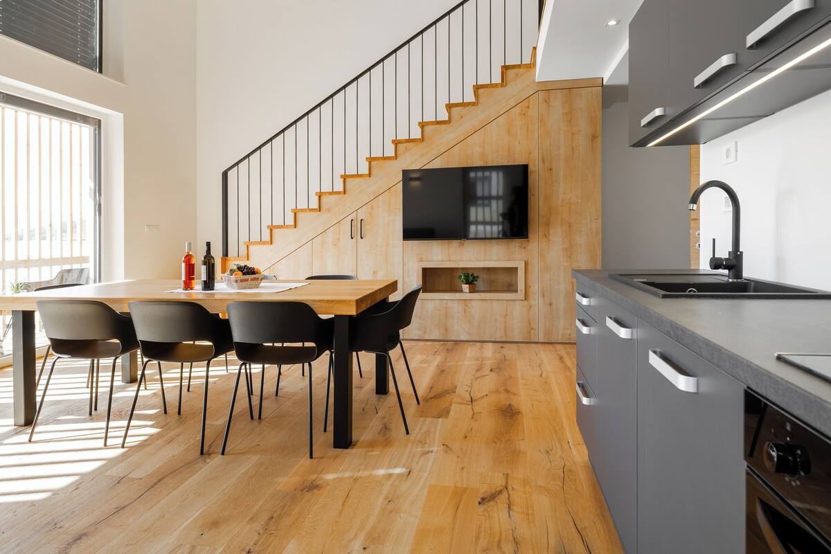 A modern kitchen with a wooden staircase, a dining area with chairs, and a built-in TV.
