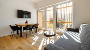A modern living room with a wooden dining table, black chairs, a grey sofa, and a TV mounted on the wall. - Winery and Apartments Marof (Bistrica ob Sotli)