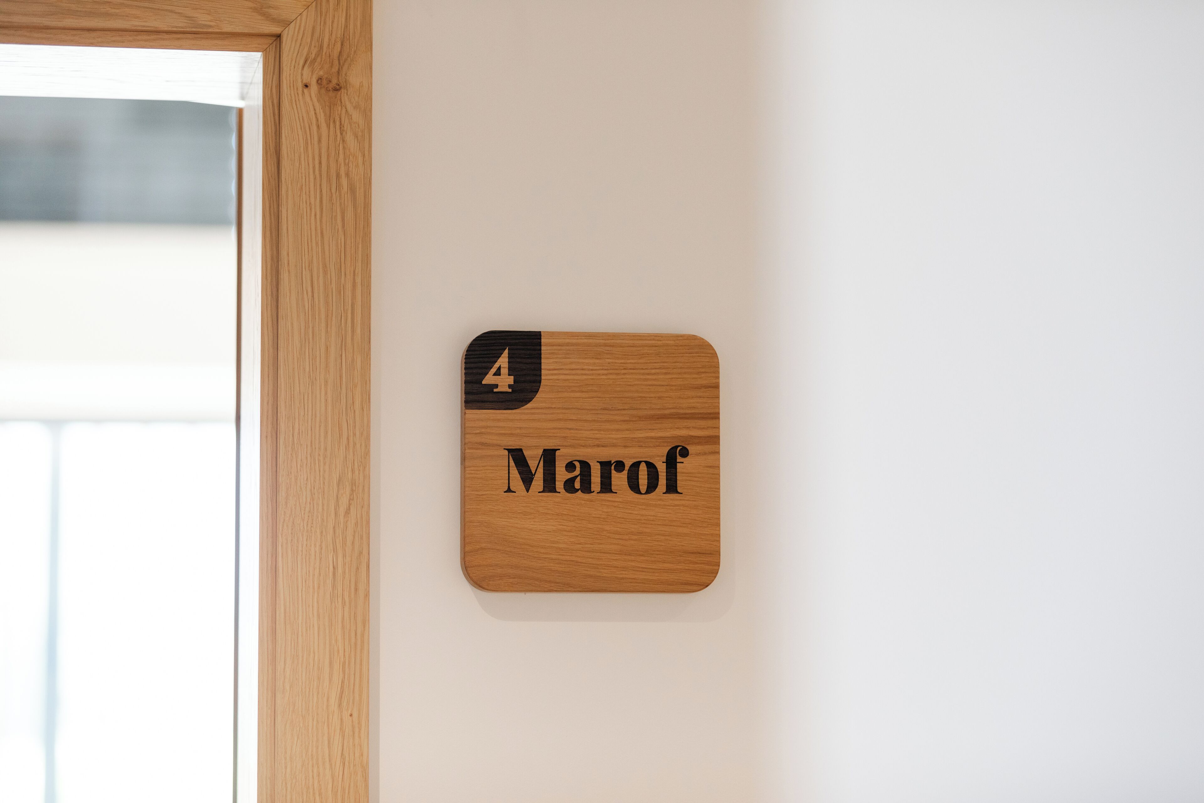 Une plaque nominative en bois, portant le numéro 4 et le nom « Marof », est fixée à un mur blanc.
