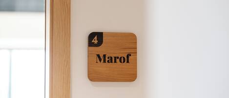 Une plaque nominative en bois, portant le numéro 4 et le nom « Marof », est fixée à un mur blanc.