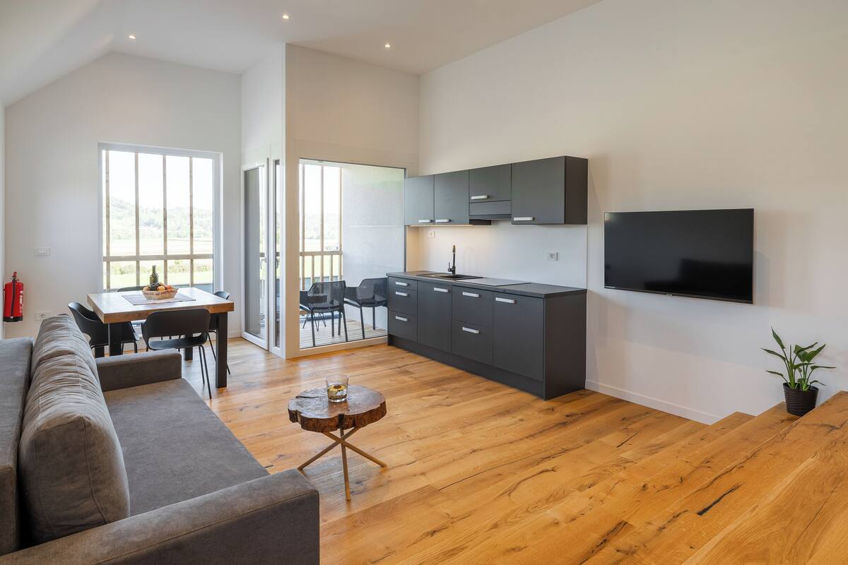 A modern living room with a sofa, a dining table, and a kitchen area with grey cabinets and a TV.