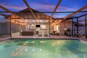 Un área de piscina techada con zona de estar, una parrilla y un televisor.