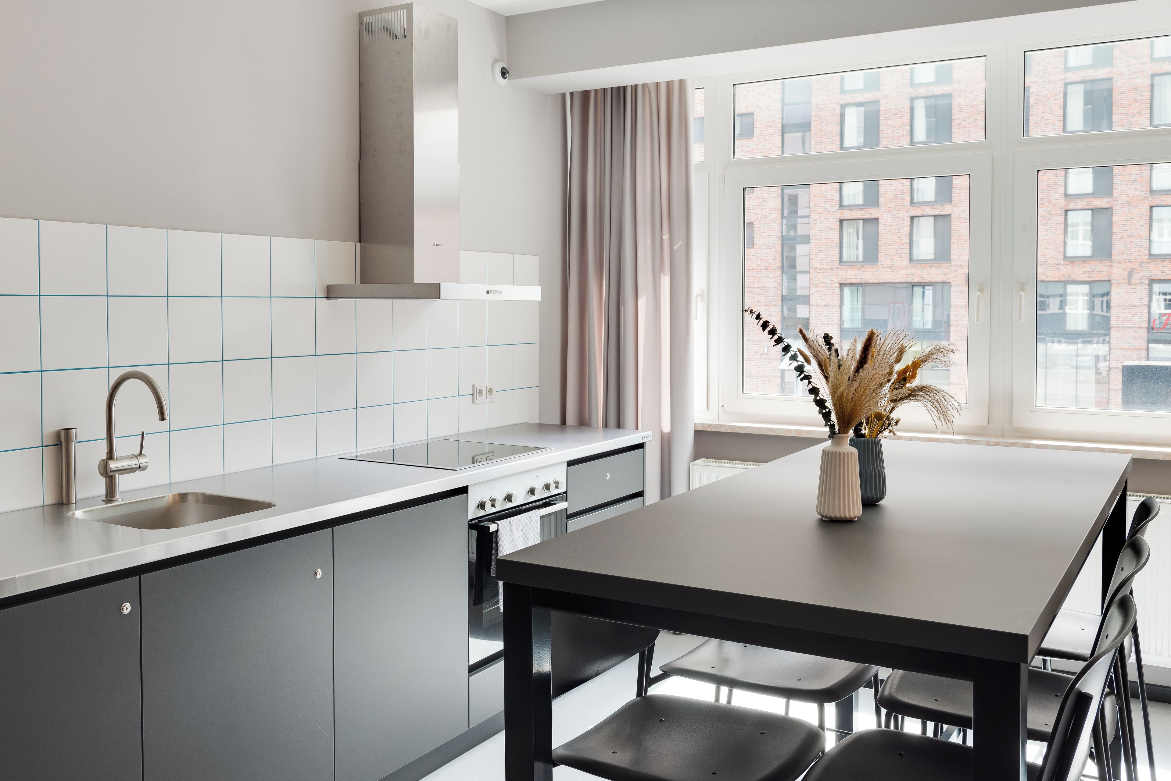 Een moderne keuken met een inbouwoven, een roestvrijstalen spoelbak en een eethoek met een tafel en stoelen.