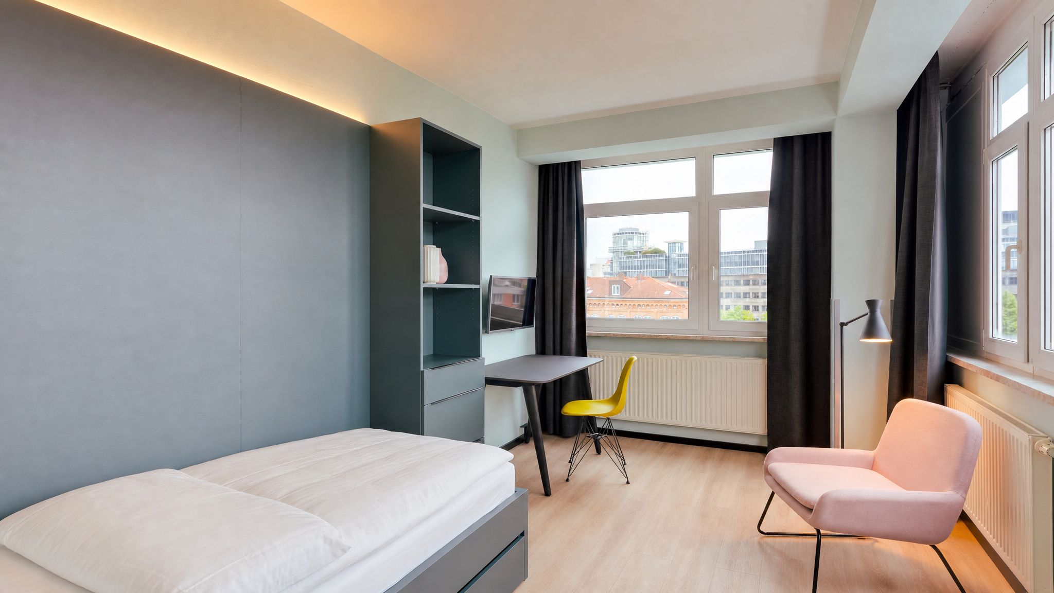 A hotel room with a bed, a desk, a chair, a TV, and a window with curtains.