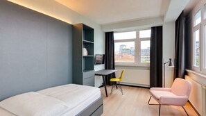 A hotel room with a bed, a desk, a chair, a TV, and a window with curtains. - MIAMI HOUSE by Homaris (Hamburg)