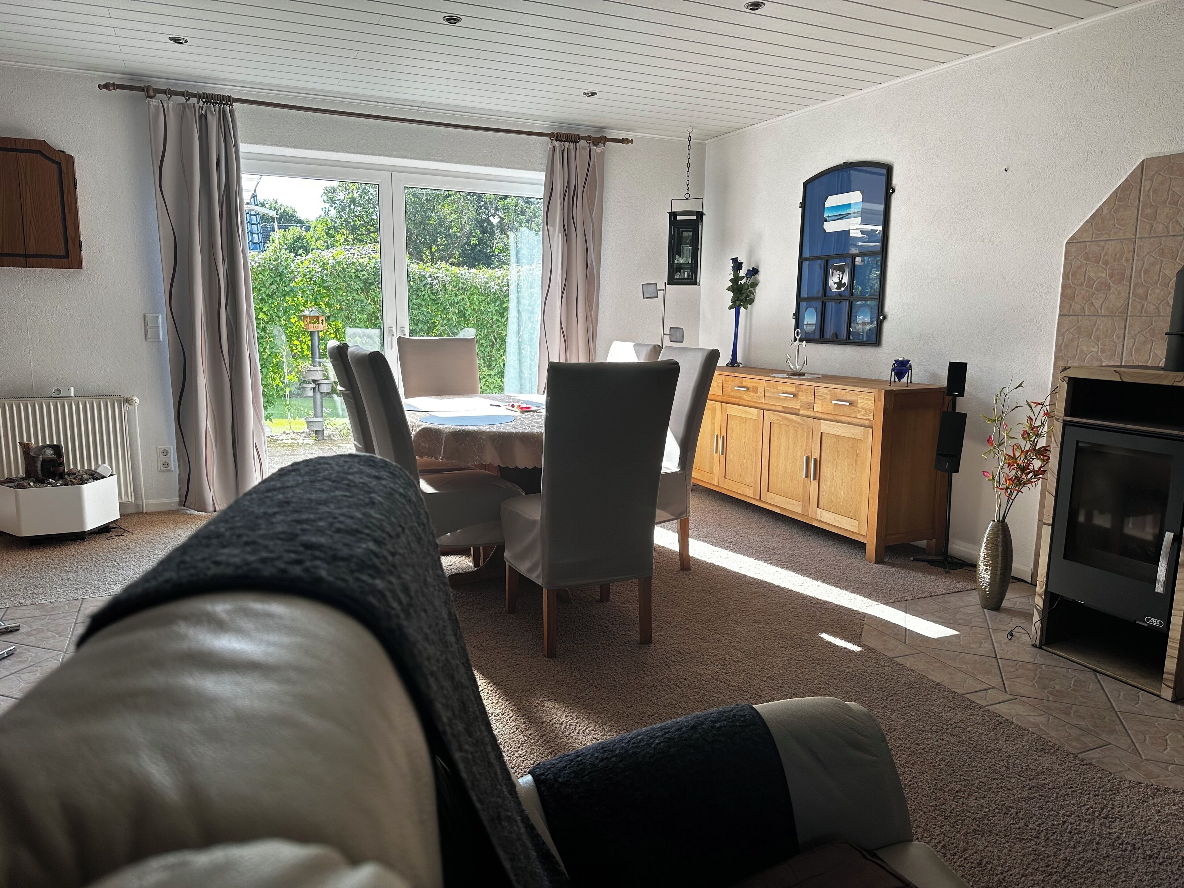Ein gemütliches Wohnzimmer mit Kamin, einem Essbereich mit Tisch und Stühlen und Blick auf den Garten durch große Fenster.