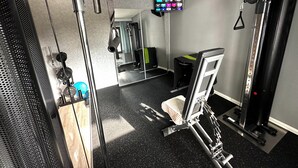 Un gimnasio con equipo de ejercicio, un espejo y una pantalla de televisión mostrando un programa de acondicionamiento físico.