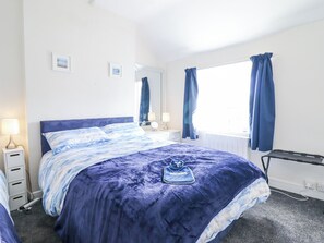 A bedroom with a bed, bedside tables, a mirror, and a window with curtains. - Minffordd (Abergele)