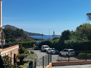 Une rue côtière bordée de voitures garées, un ciel bleu dégagé et un paysage vallonné en arrière-plan.