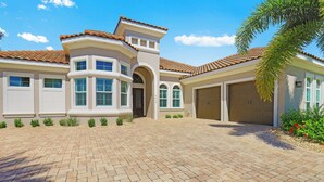 A two-story house with a brick driveway, a garage, and a covered patio area.