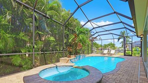 An indoor swimming pool with a hot tub, surrounded by a glass enclosure and tropical plants.