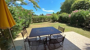 Une terrasse extérieure avec une table et des chaises, entourée d’une végétation luxuriante et de plantes en fleurs.