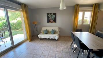 Un coin repas avec une table et des chaises, un canapé avec des coussins, une lampe sur pied et un tableau au mur.