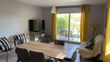 Un salon moderne avec une table à manger en bois, des sièges confortables, un téléviseur à écran plat et un canapé agrémenté de coussins.
