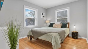 Une chambre à coucher avec un lit, deux fenêtres, une lampe de chevet et une plante.