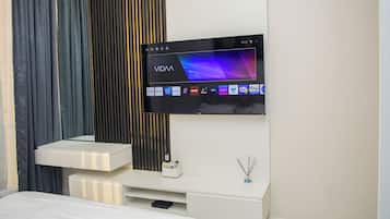 A modern hotel room with a flat-screen TV mounted on the wall, a white bedside table, and a bed with white bedding.