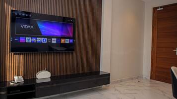 Un salon moderne avec un téléviseur à écran plat fixé à un mur en bois, un meuble de rangement intégré en dessous et un sol recouvert de carreaux de marbre.
