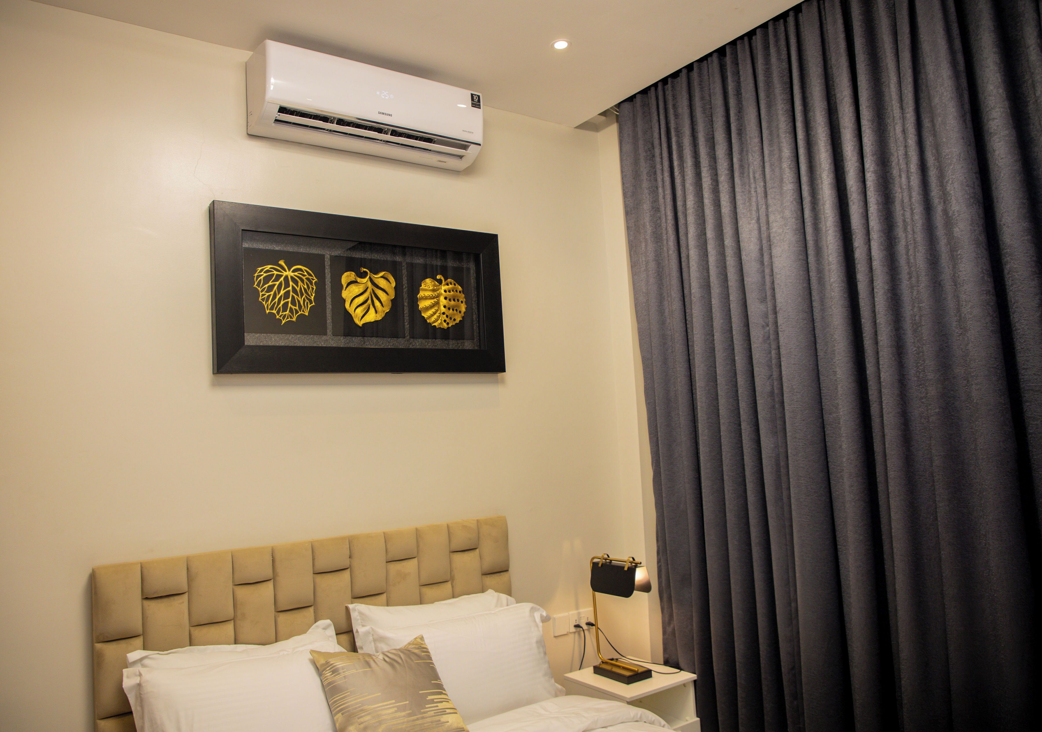A hotel room with a bed, a bedside table with a lamp, and an air conditioner on the wall.