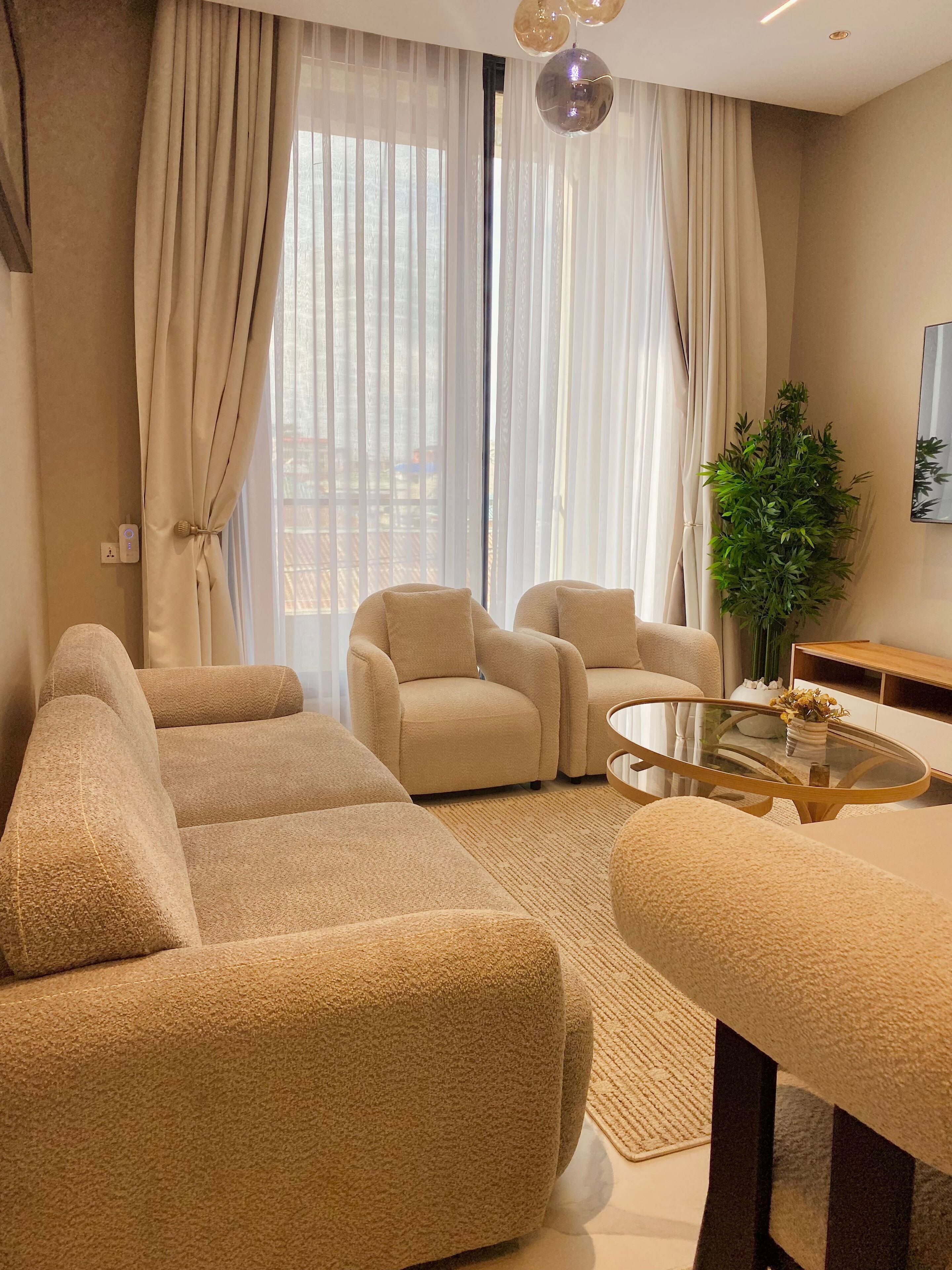 Ein modernes Wohnzimmer mit beigefarbenen Sofas, einem Glastisch und einer Topfpflanze.