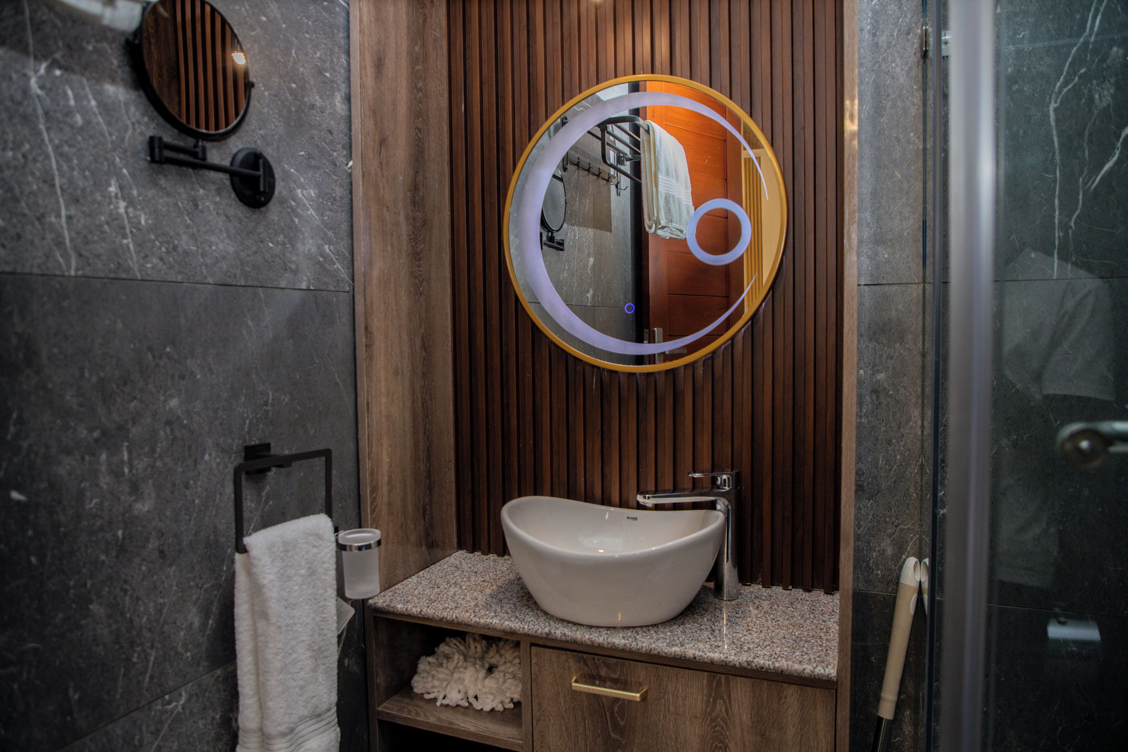 A modern bathroom with a wooden vanity, a round mirror, and a glass shower enclosure.