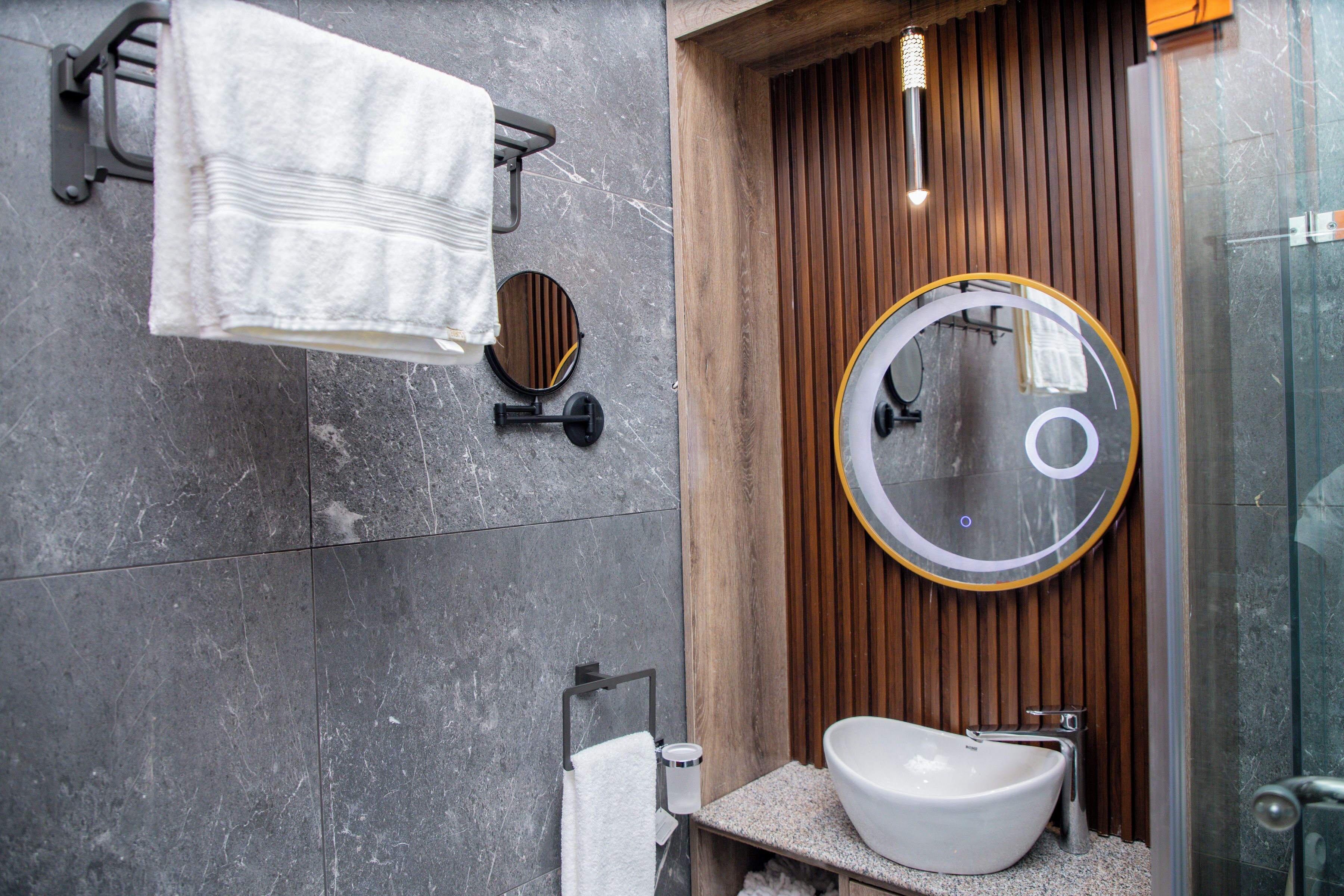 Un bany modern amb un mirall rodó, un lavabo blanc i un suport per tovalloles.