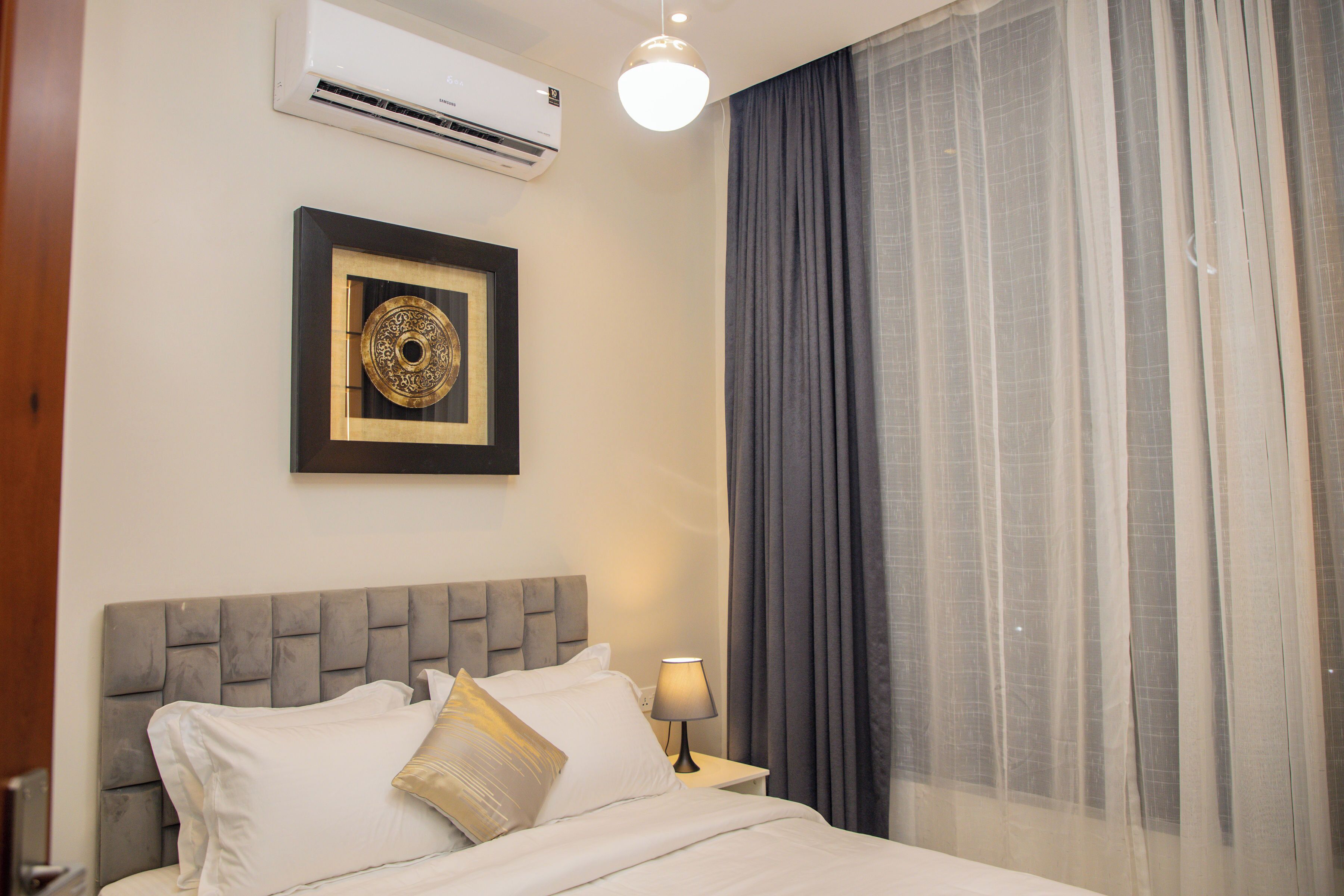A hotel room with a bed, a nightstand, a lamp, a framed picture, and a window with curtains.