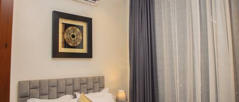A hotel room with a bed, a nightstand, a lamp, a framed picture, and a window with curtains.