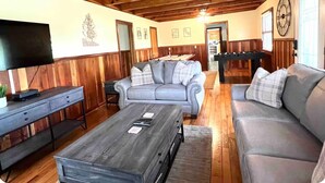 A cozy living room with a grey sofa, a wooden coffee table, and a television on a wooden cabinet. - Prime Location Cabin, Easy Access with Views,AC,WiFi 3min to Parkway (Pigeon Forge)