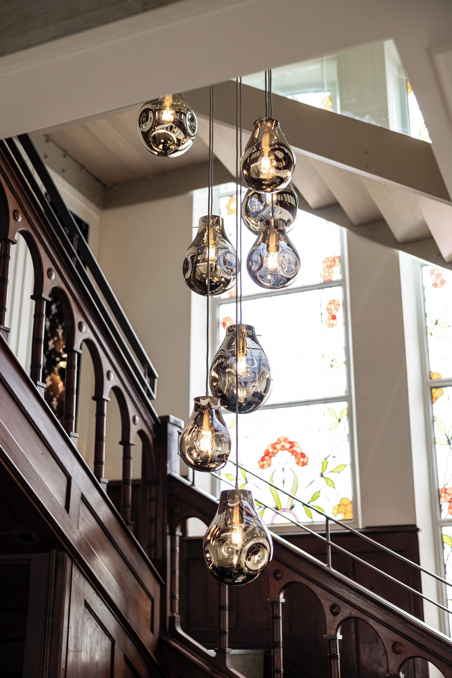 Un escalier doté d’une rampe en bois et d’un luminaire moderne équipé de plusieurs ampoules.