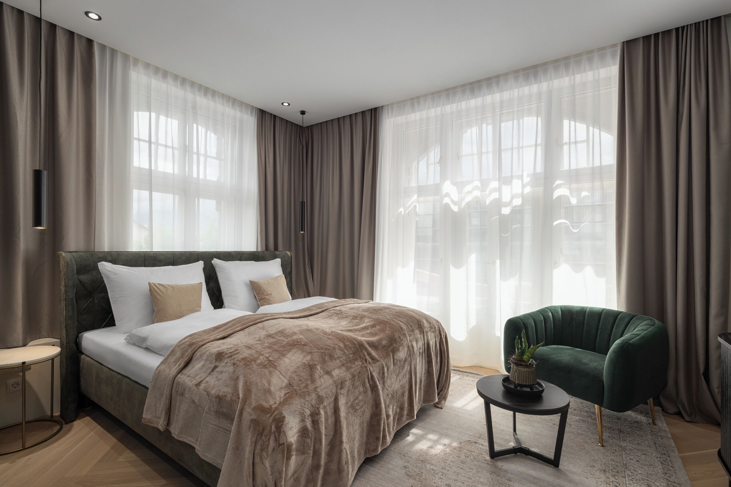 A modern bedroom with a large bed, a green armchair, and a small side table.