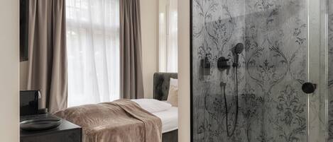 Una habitación de hotel moderna con cama, mesita de noche, escritorio y ducha con puerta de vidrio.