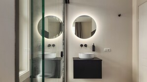 Un baño moderno con dos espejos redondos, un lavabo blanco y un mueble de tocador negro.