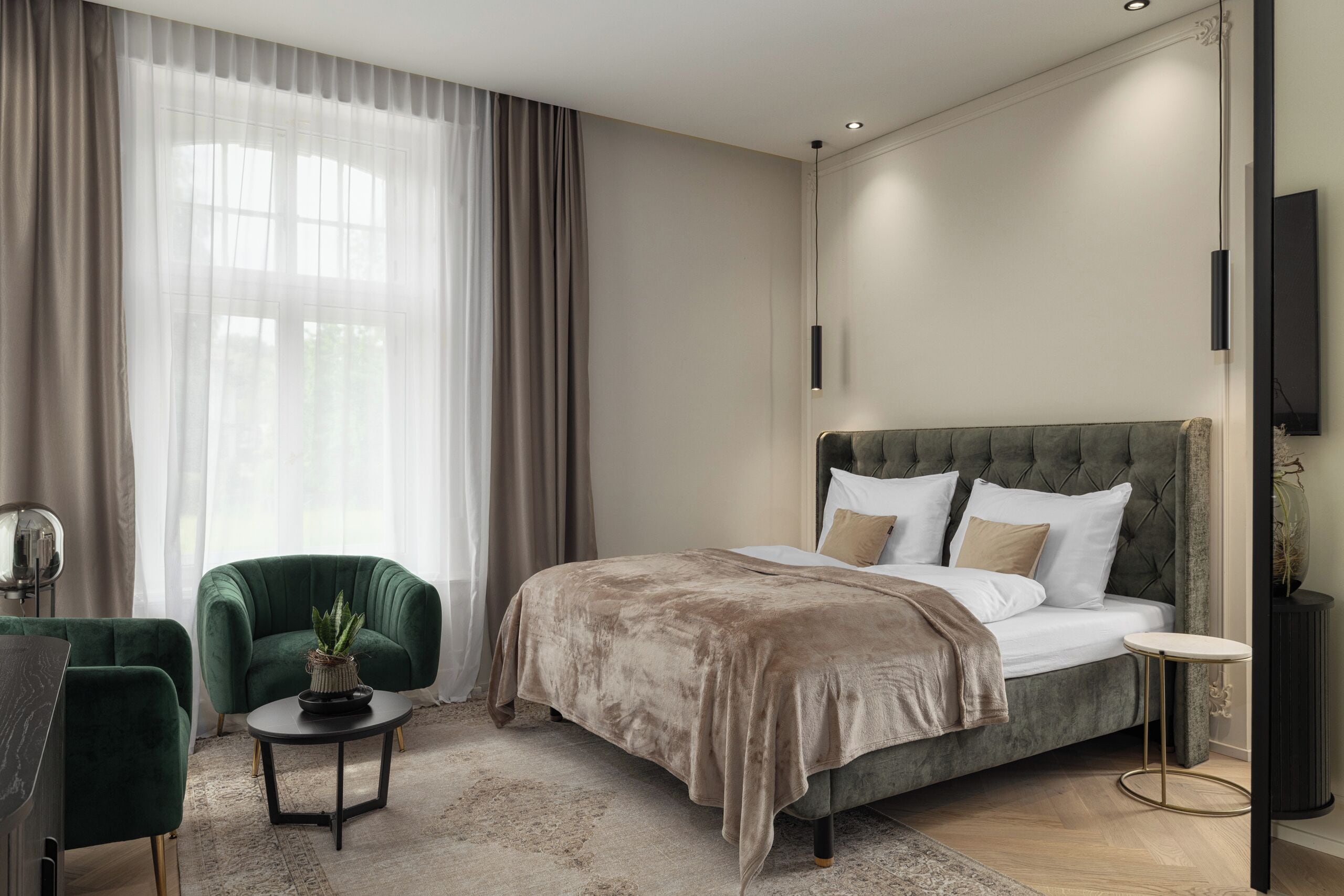 A modern bedroom with a large bed, a green armchair, a small table, and a TV.