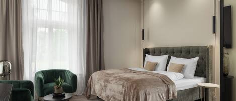 A modern bedroom with a large bed, a green armchair, a small table, and a TV.