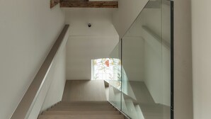 Una escalera moderna con escalones de madera y barandillas de vidrio, que conduce a un rellano con un ventanal decorativo de vitral.