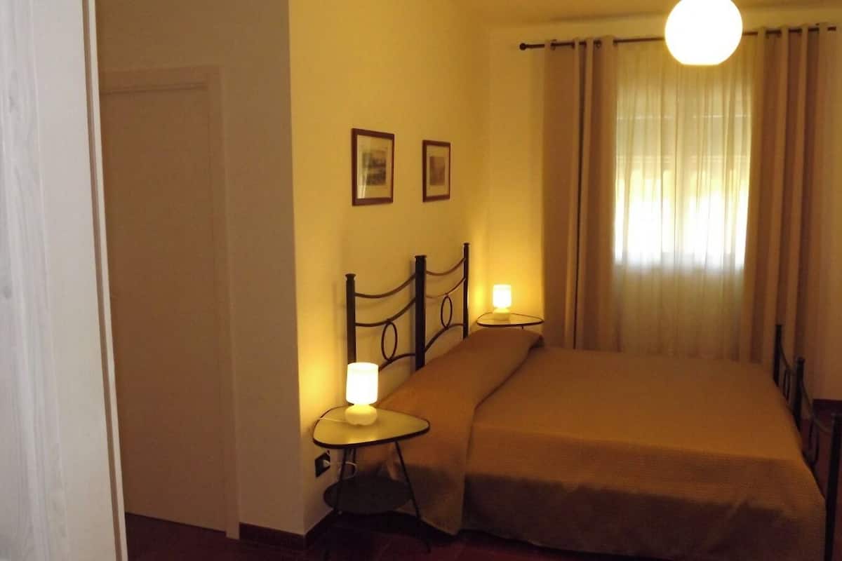Une petite chambre à coucher accueillante, avec un lit simple, une table de chevet avec une lampe et un tableau accroché au mur.