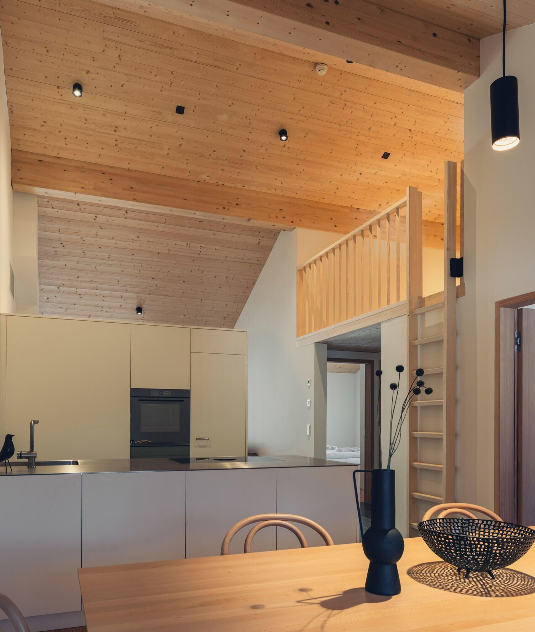 Cocina moderna con vigas de madera en el techo, zona de comedor con mesa de madera y vista al espacio de la sala.