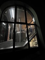 Vista a través de un amplio ventanal de una estación de metro con escaleras mecánicas de metal e iluminación de estilo industrial.